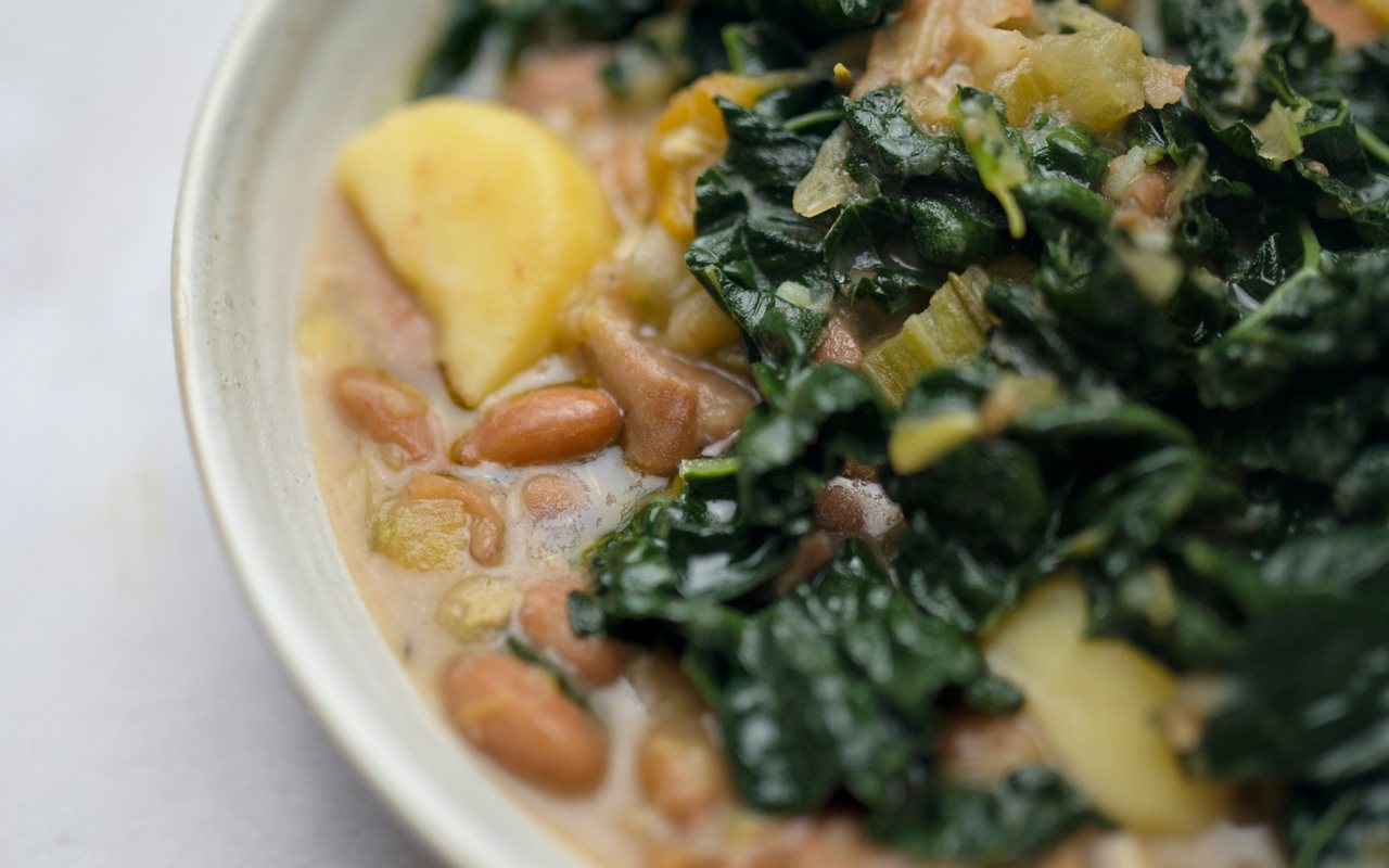 A close-up bowl of cranberry bean soup with kale and potato pieces.