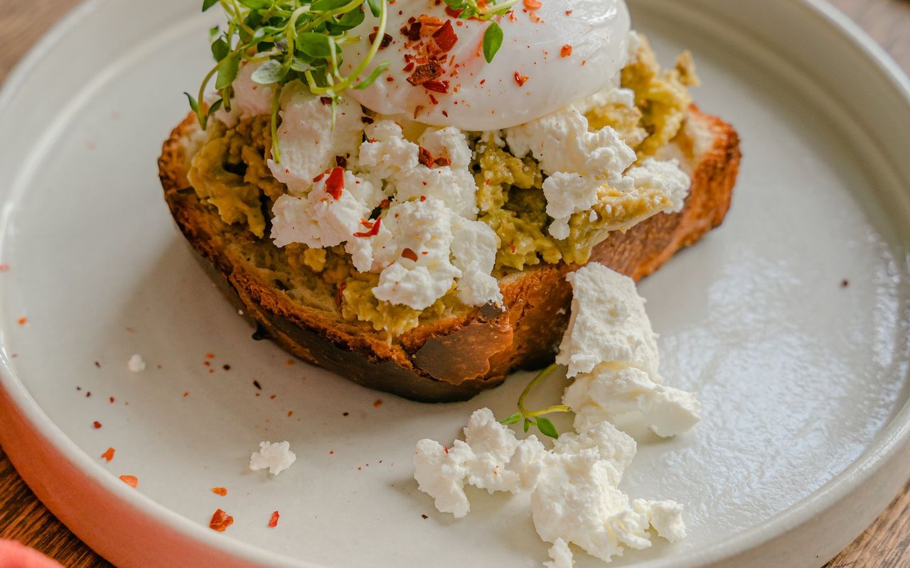 Avocado toast topped with sliced egg, cherry tomatoes, and herbs