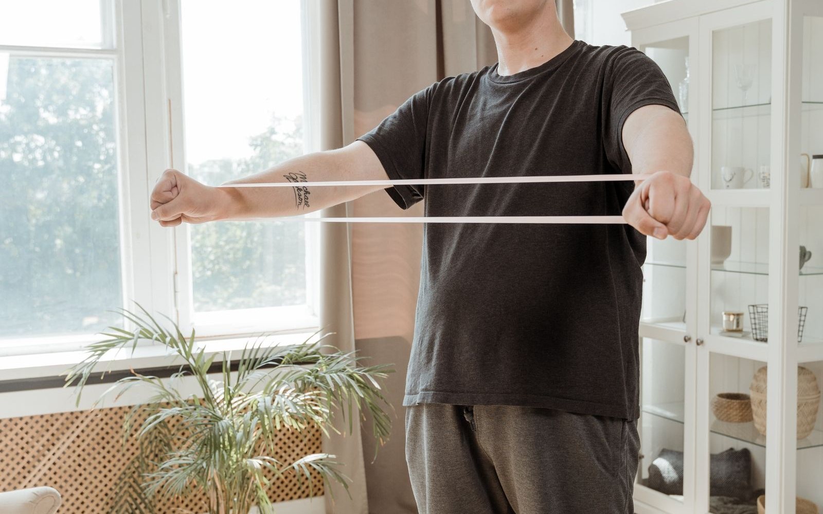Person performing a light resistance-band exercise in a bright room.