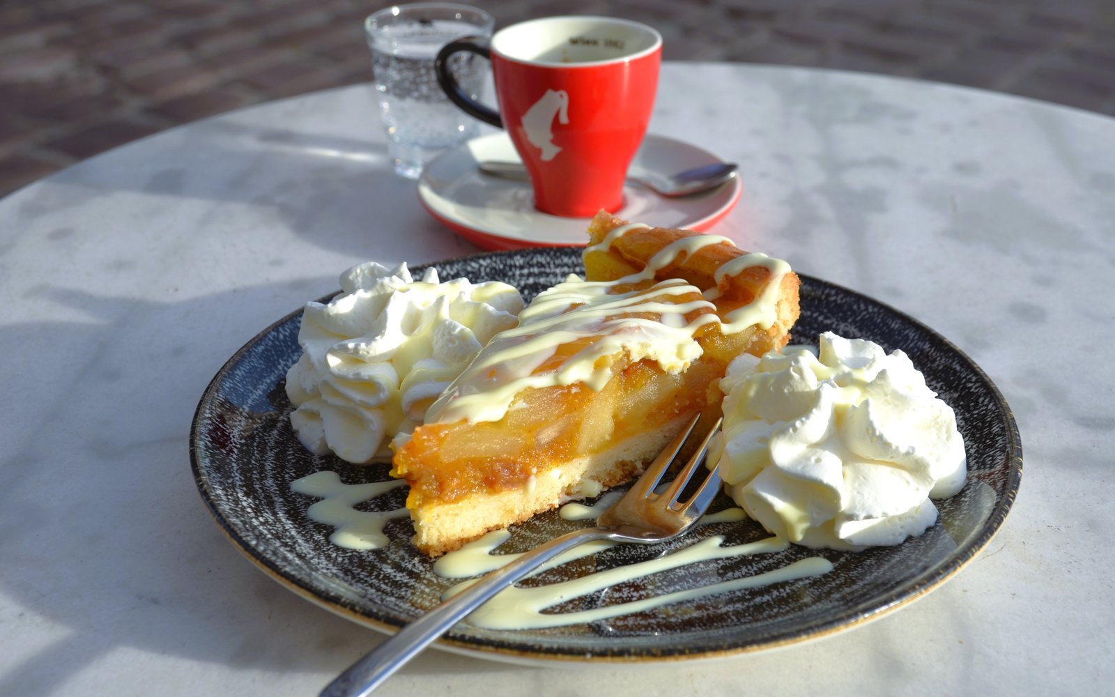 Slice of apple pie with whipped cream beside coffee and water.