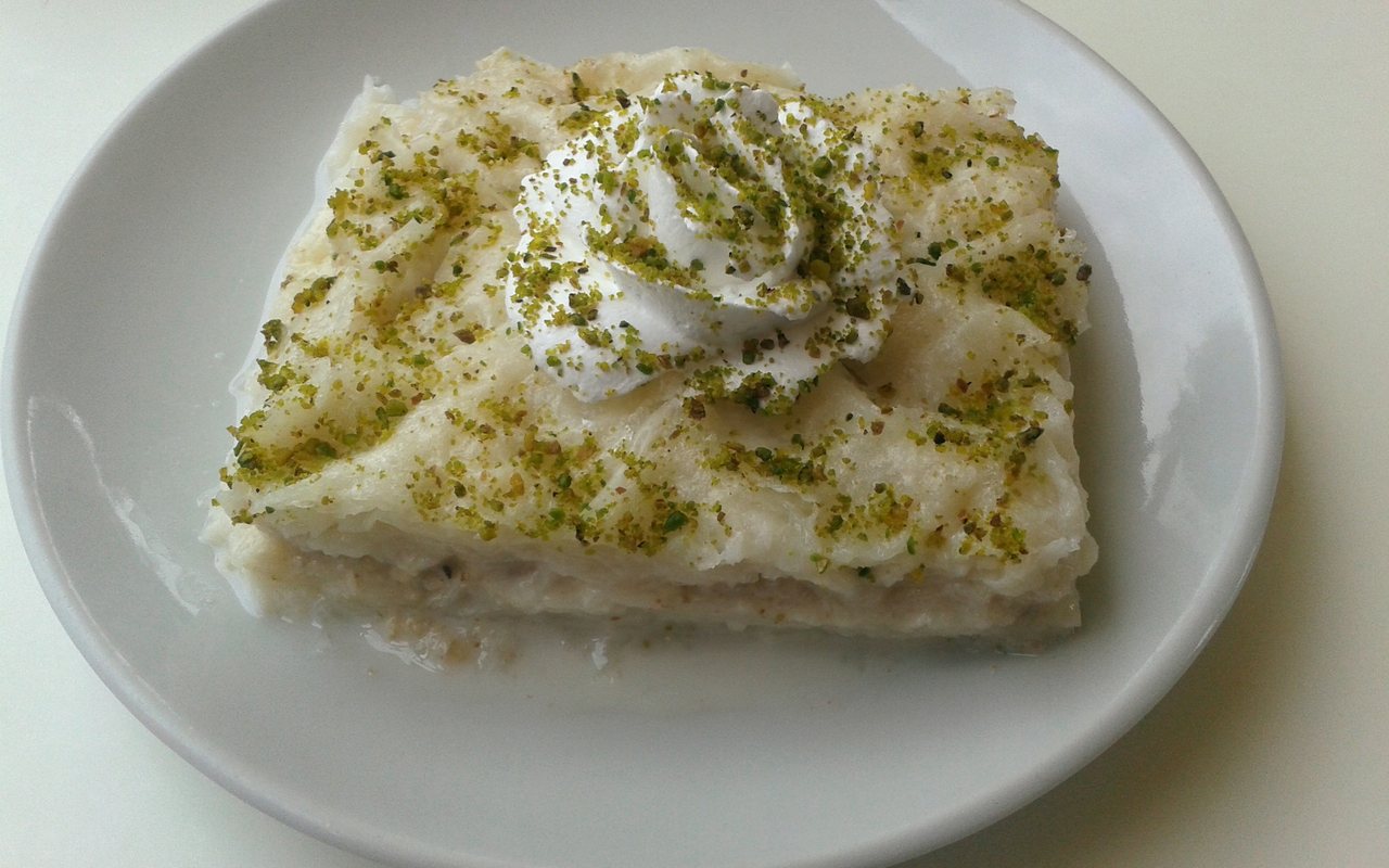 Square slice of layered güllaç topped with a whipped-cream rosette and ground pistachios