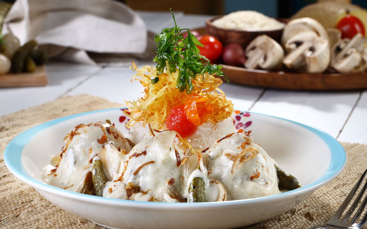 Cream-sauced mushroom dish served with white rice, crisp potato strands, and a cherry tomato garnish