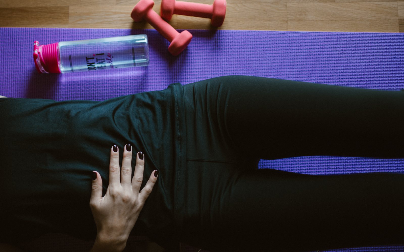 Adult rests on a purple exercise mat beside pink dumbbells and a water bottle.