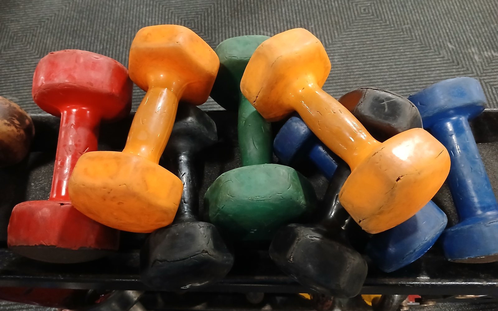 Pile of red, orange, green, blue, and black dumbbells on a gym rack.