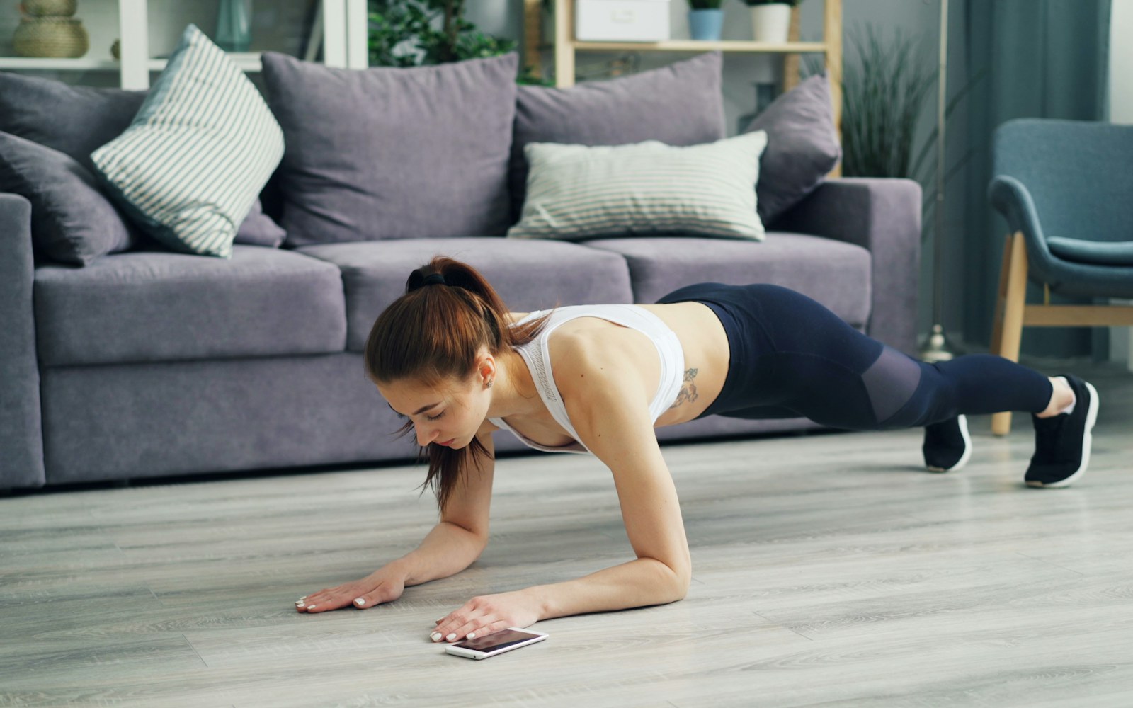 Woman holds a plank during a home workout beside her phone
