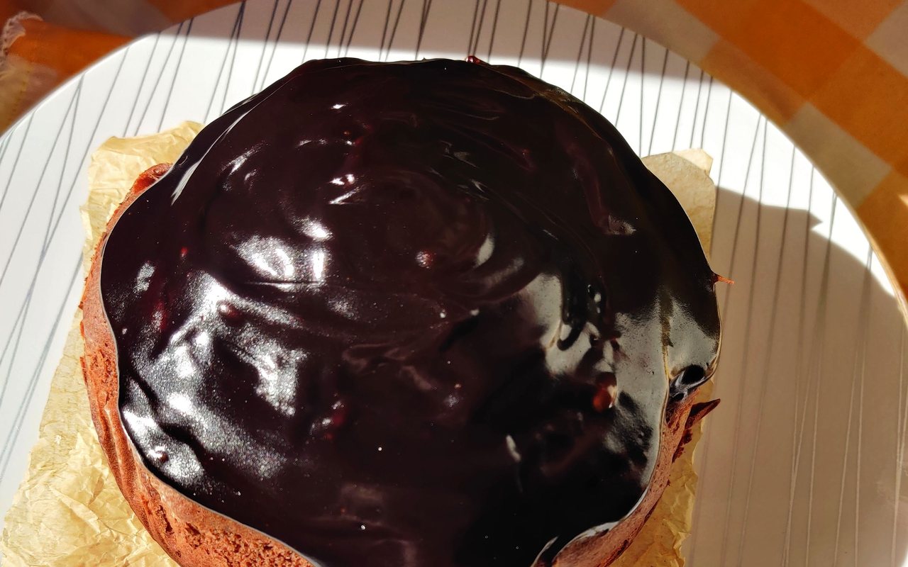 Chocolate cake coated with glossy dark ganache on a lined plate