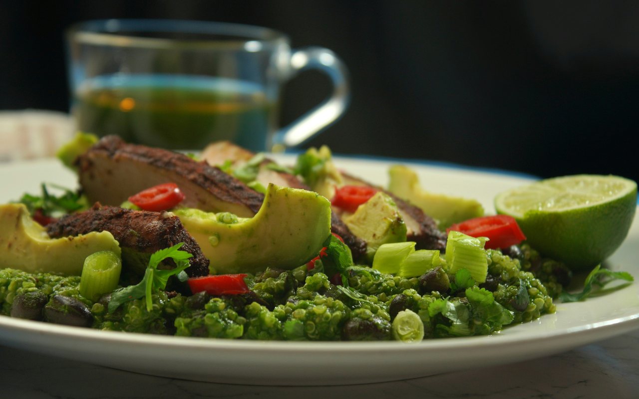 Grilled chicken pieces with green quinoa, avocado, cherry tomatoes, scallions, herbs, and a halved lime on a white plate.