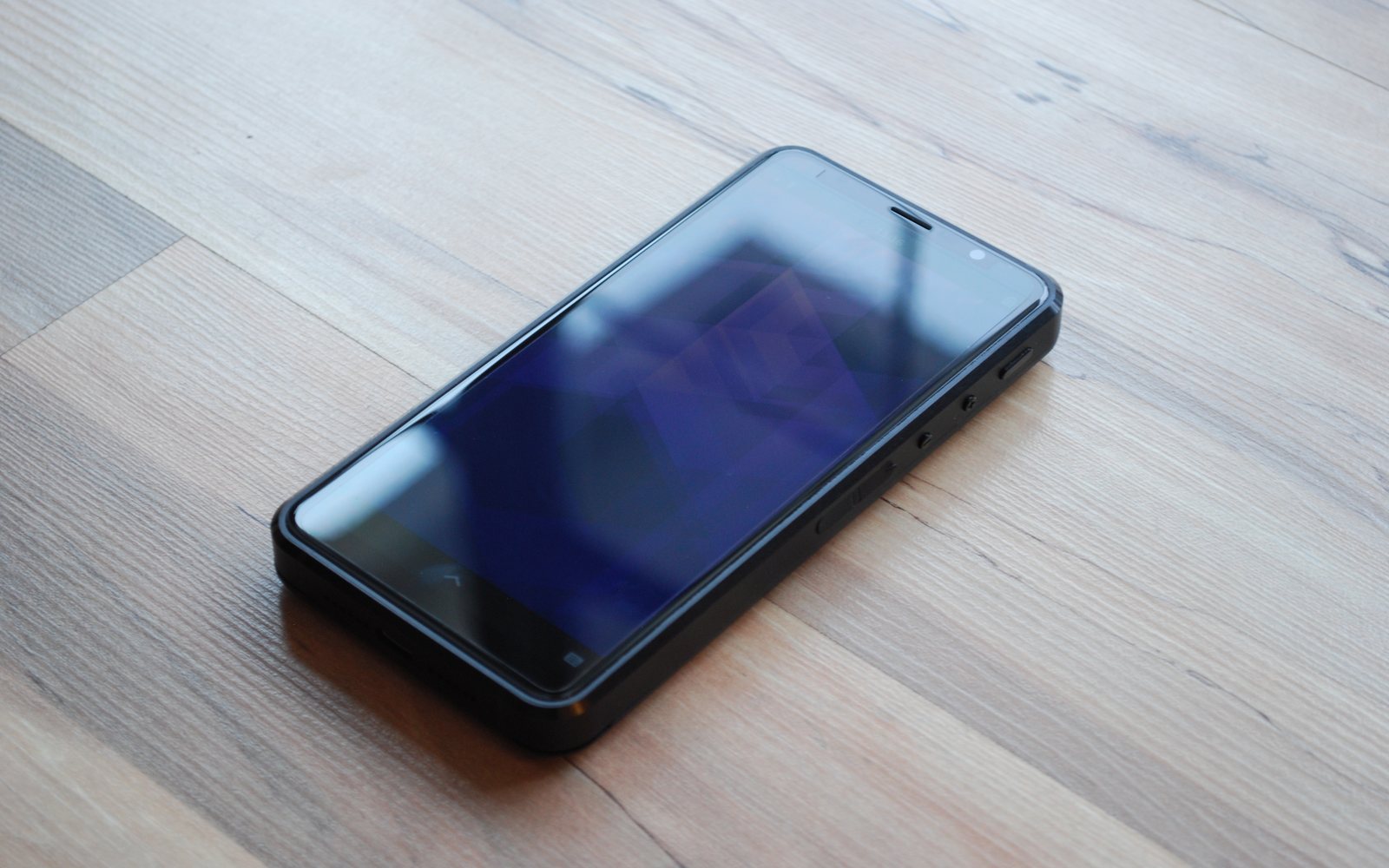 Smartphone with a dark reflective screen resting on a wooden floor.