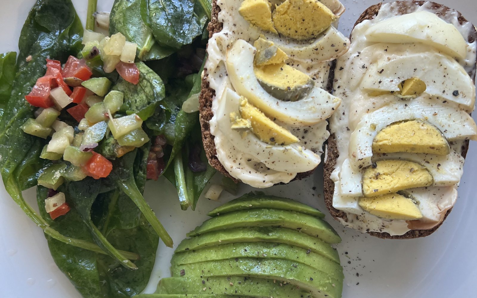 Egg-topped bread, sliced avocado, and leafy salad arranged on a plate.