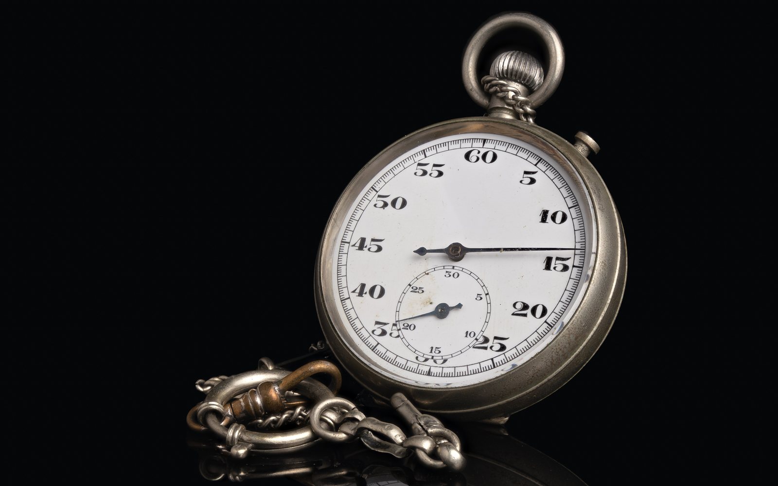 Antique stopwatch with a metal chain against a black background.
