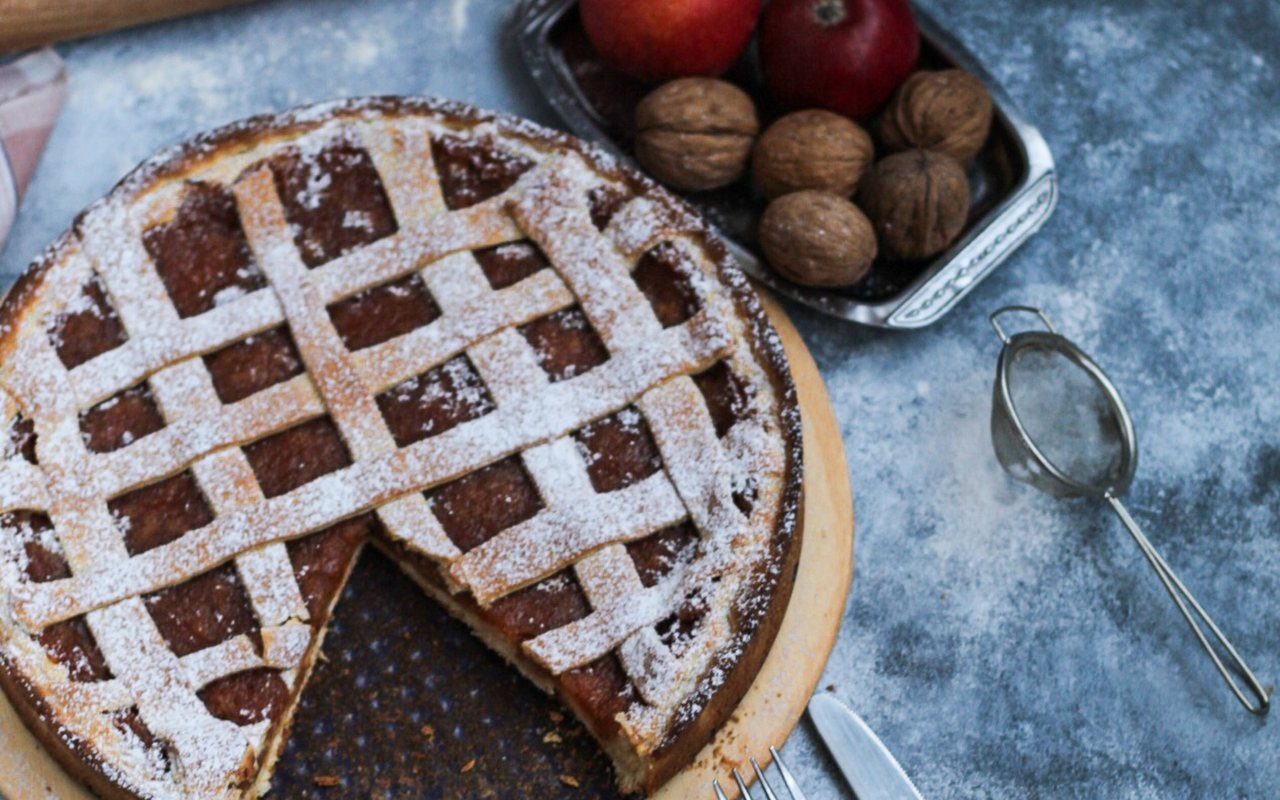 A powdered-sugar-dusted lattice tart beside whole walnuts and red apples