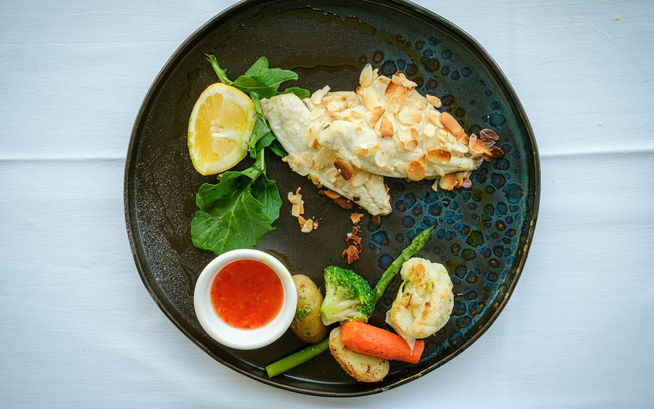 Almond-crusted fish fillet with potatoes, broccoli, asparagus, cauliflower, carrots, and red sauce.