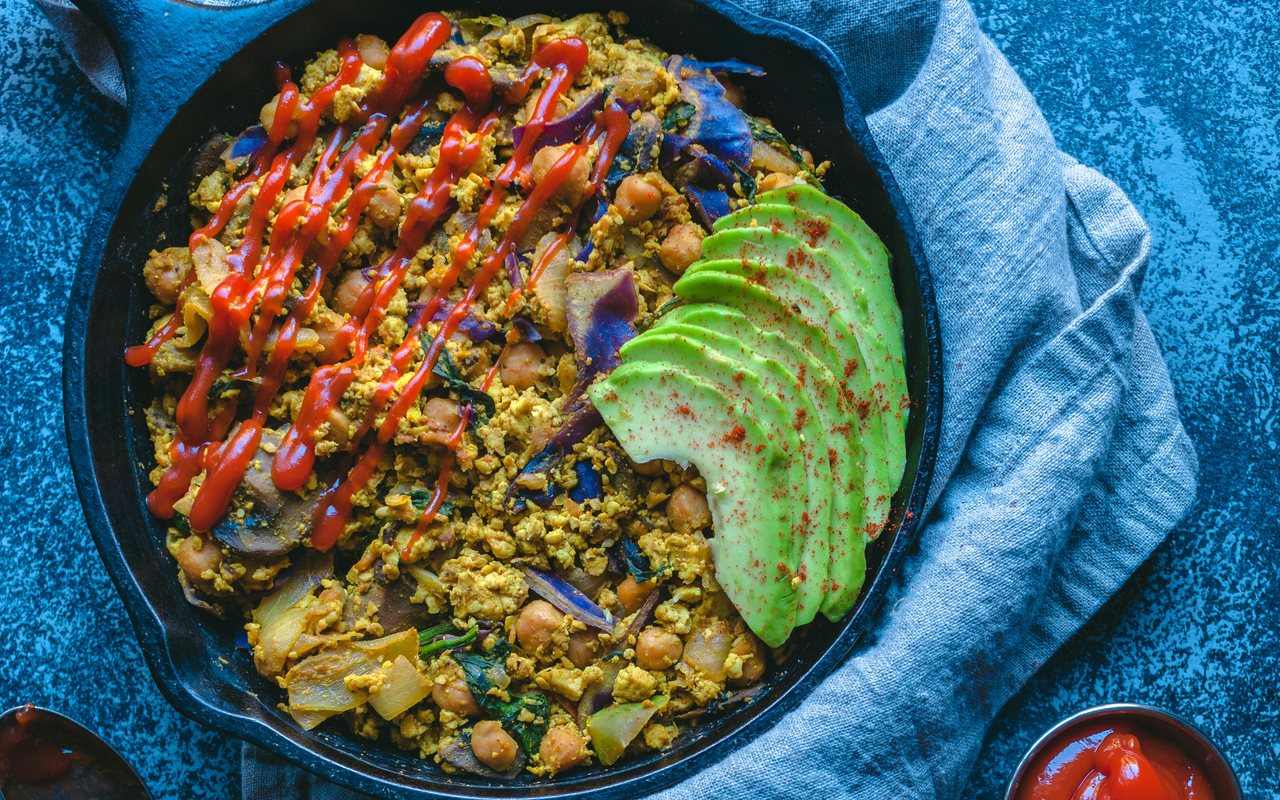 A skillet of tofu scramble with chickpeas, red cabbage, onions, spinach, avocado, and red sauce.