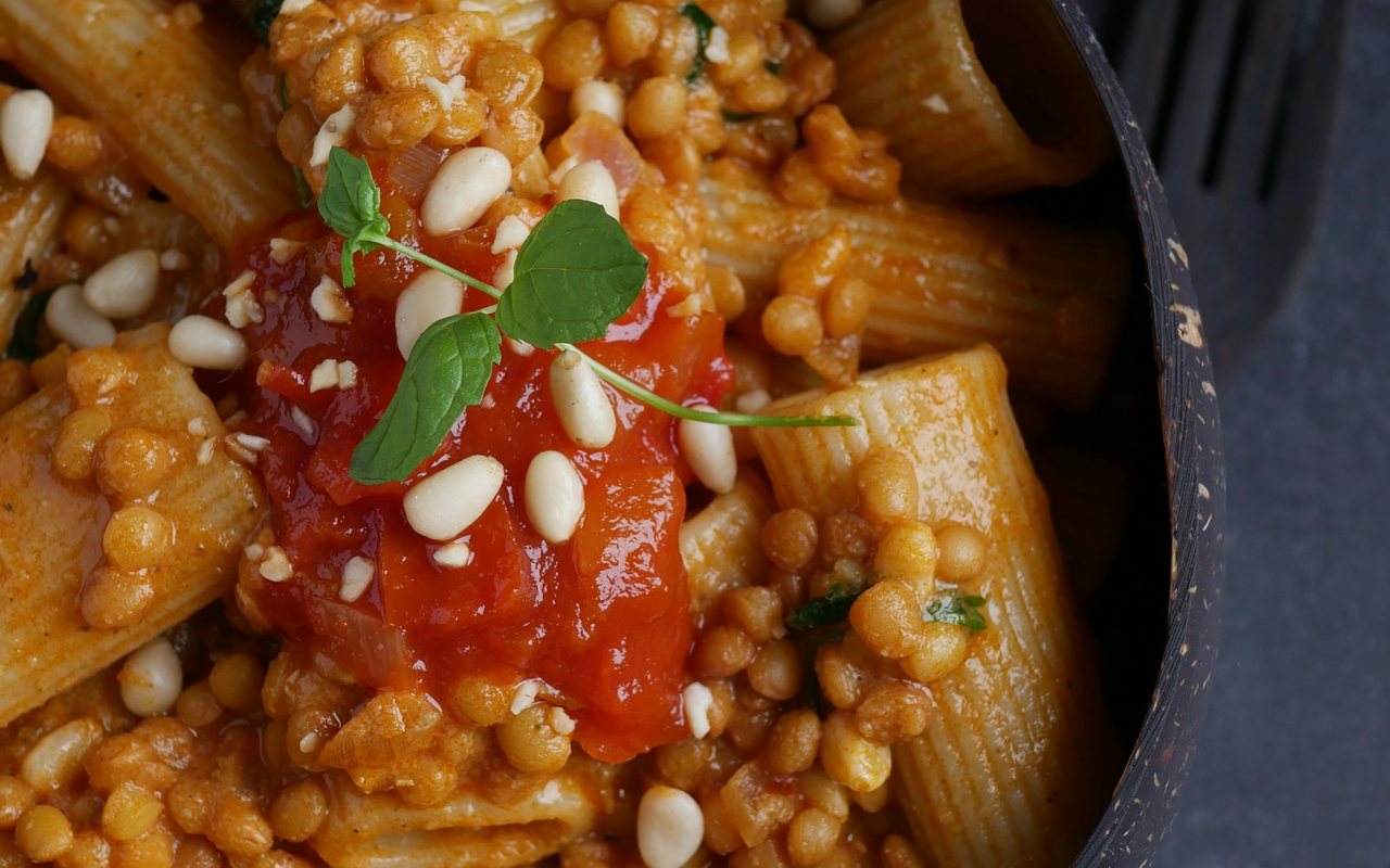 Tomato-coated lentil rigatoni with pine nuts and mint in a dark bowl.