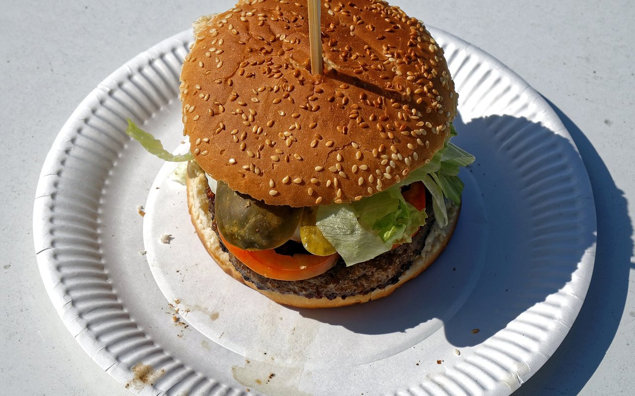 Two homemade hamburgers in sesame-topped buns with lettuce, tomato, onion, and cheese