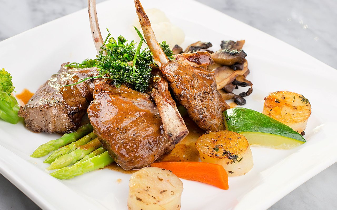 Glazed lamb chops with roasted potato rounds and green vegetables on a white plate