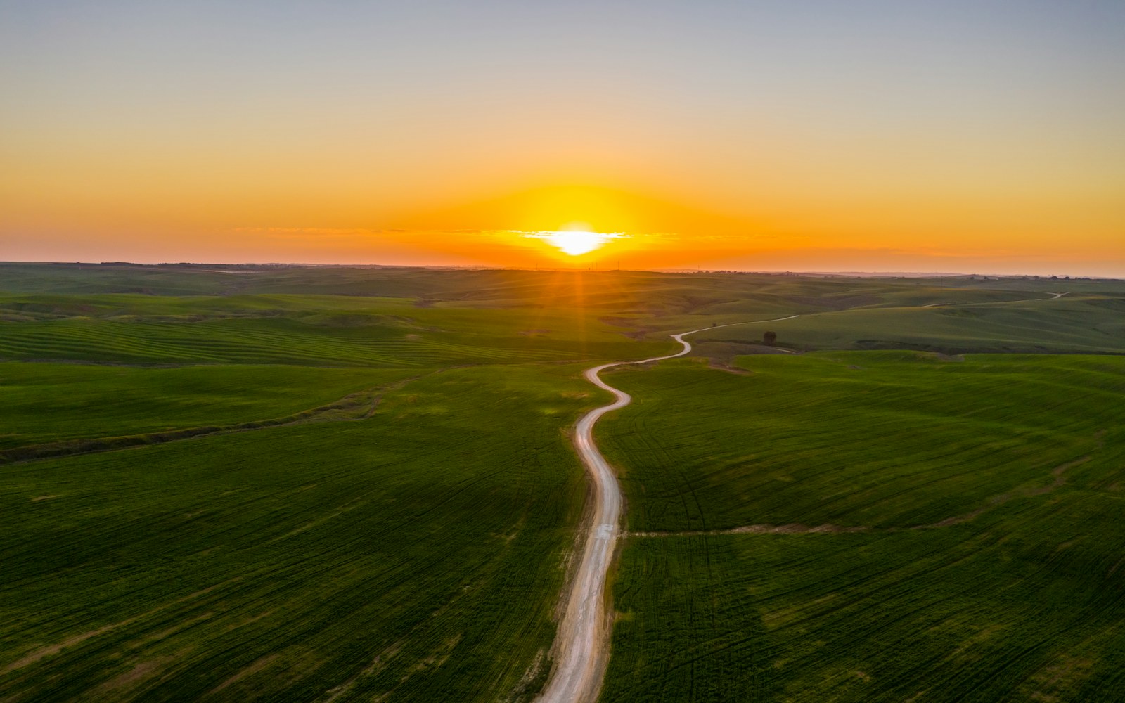 Aerial view of a winding road through green fields at sunset