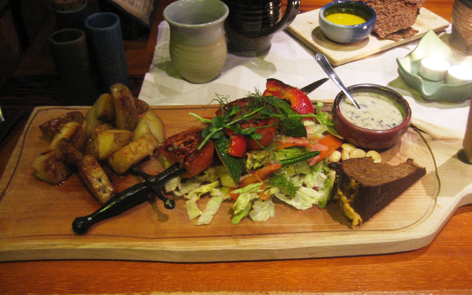 Restaurant plate with roasted potatoes, salad, vegetables, bread, and dipping sauce.