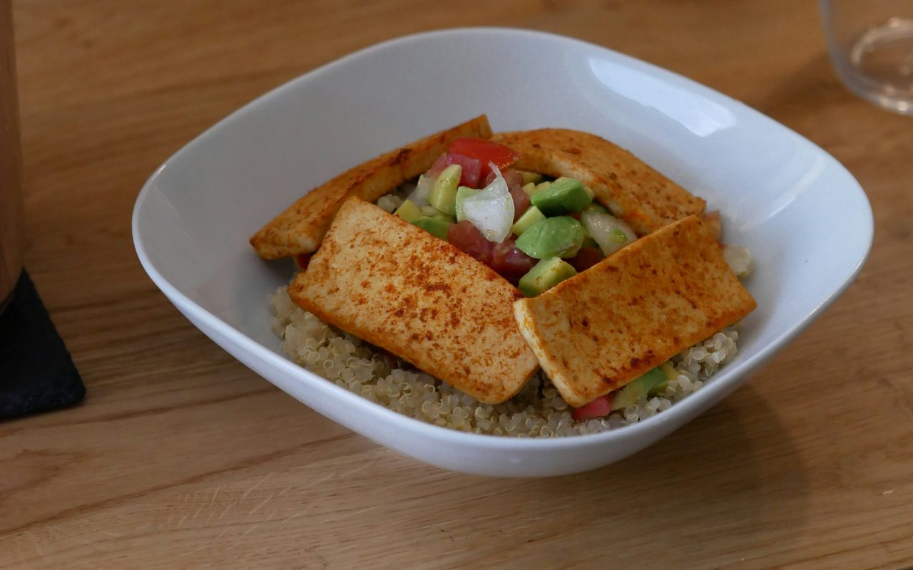 Quinoa bowl with browned tofu, avocado, tomatoes, red onion, and herbs.