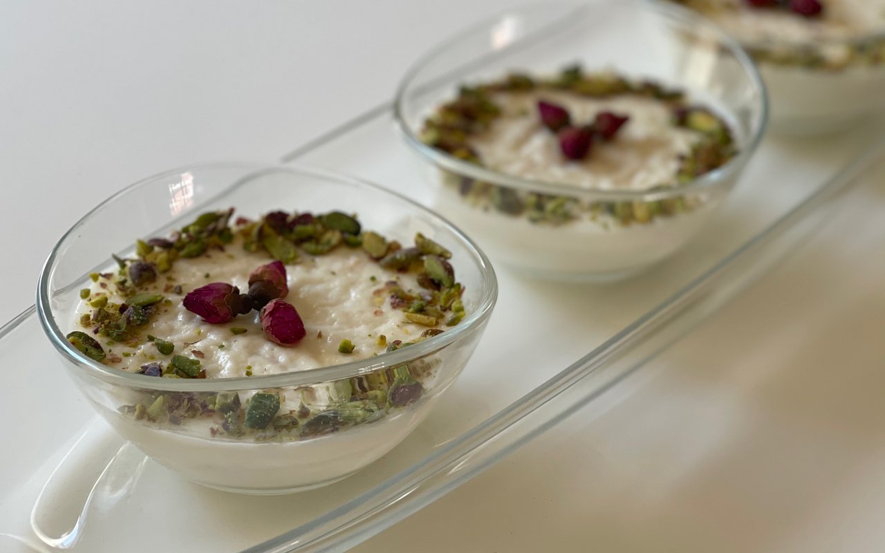 White milk puddings in glass bowls garnished with pistachios and rose petals