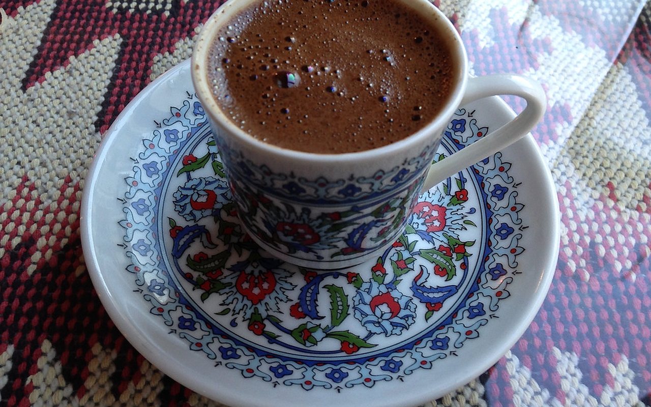 Two small cups of dark Turkish coffee with foam on top beside a copper cezve