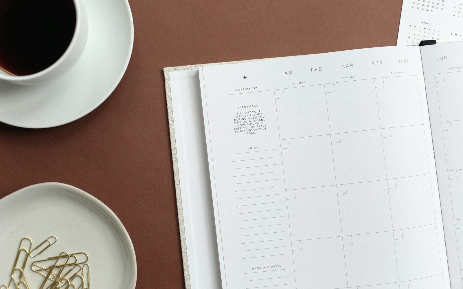 Open planner beside a cup and a dish of paper clips