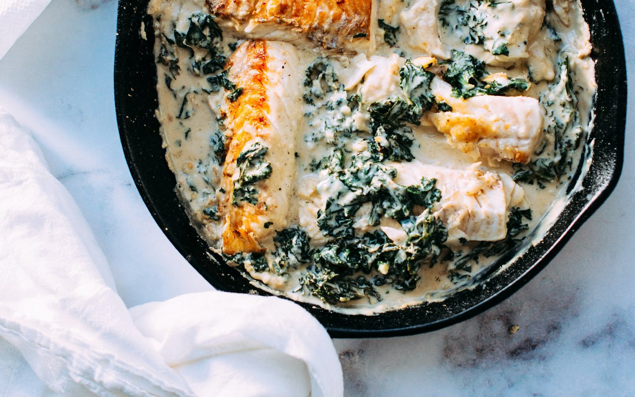 White fish fillets in a creamy kale sauce in a black skillet.