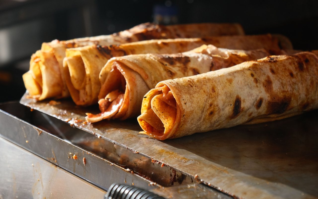 Rolled flatbreads with reddish filling browning on a metal griddle