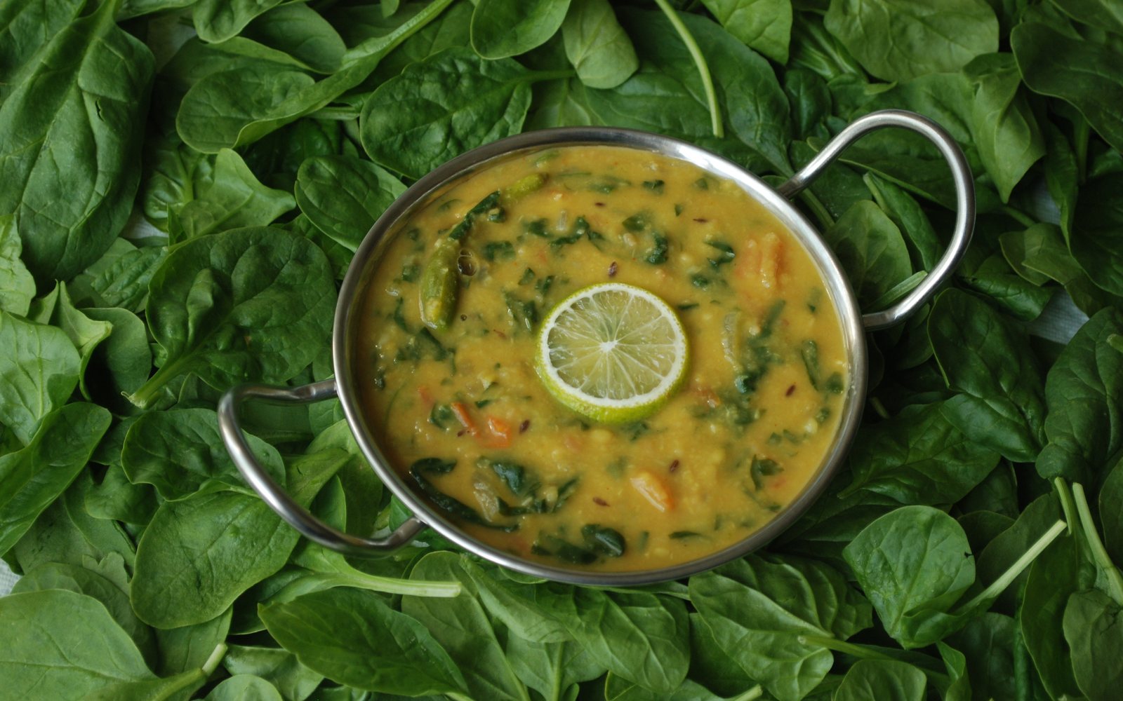 Bowl of lentil and spinach curry served over fresh spinach leaves.
