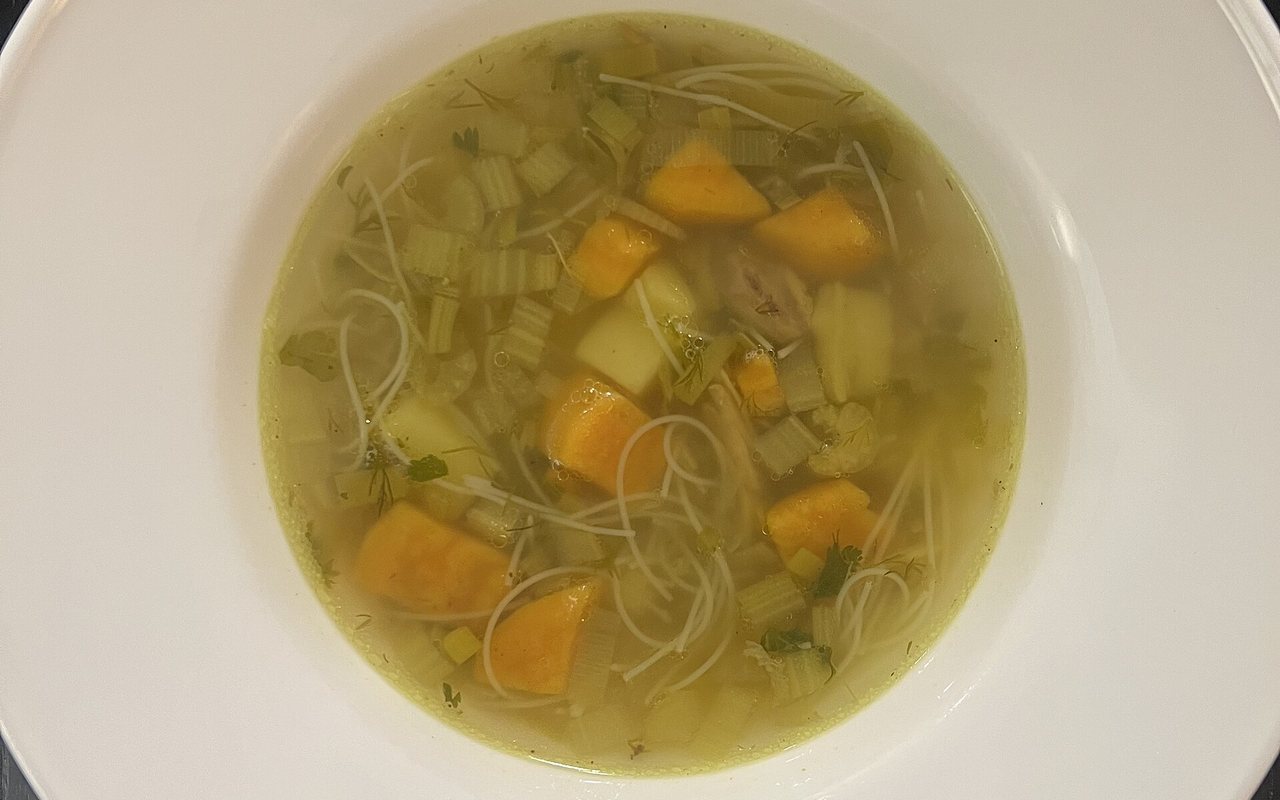 Golden chicken soup with shredded chicken and carrot in a white bowl
