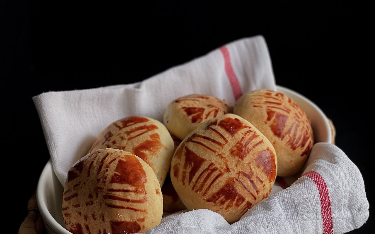 Round golden cheese-filled poğaça topped with sesame and nigella seeds on a baking tray