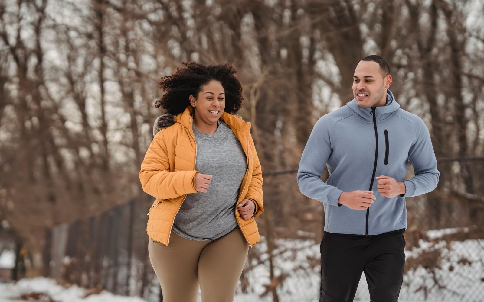 Two adults smile and talk while jogging together through a winter park.