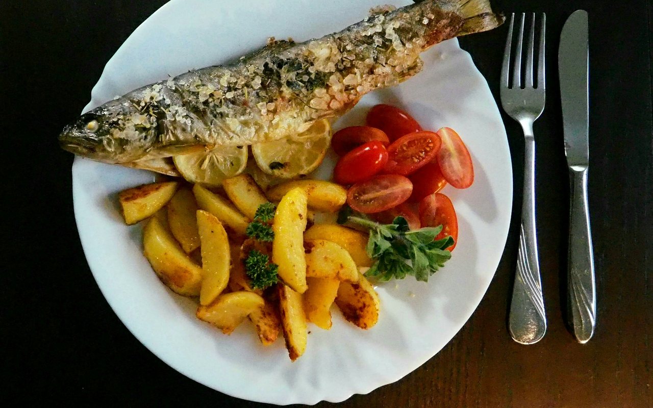 Whole cooked fish with roasted potato wedges, tomatoes, lemon, and herbs.