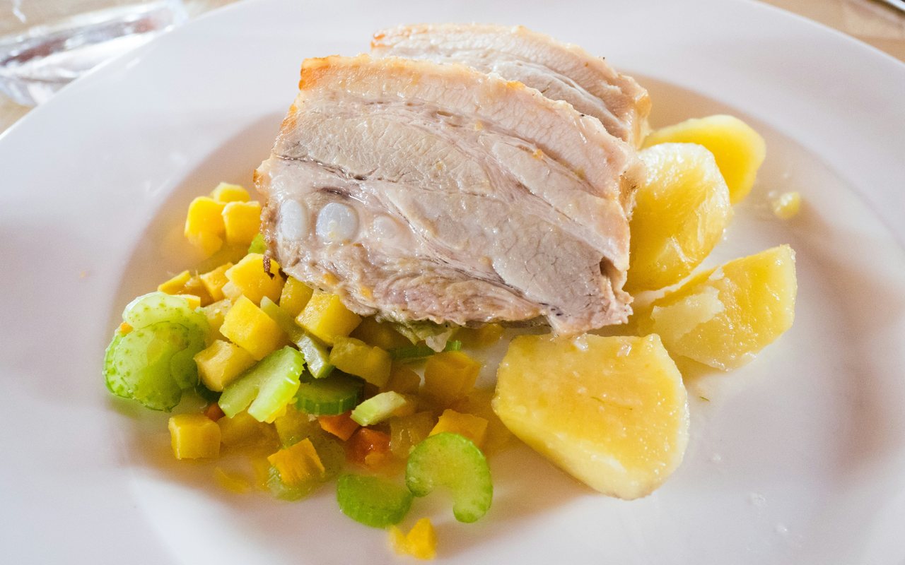 Sliced roast pork with potatoes, carrots, celery, onions, and herbs.