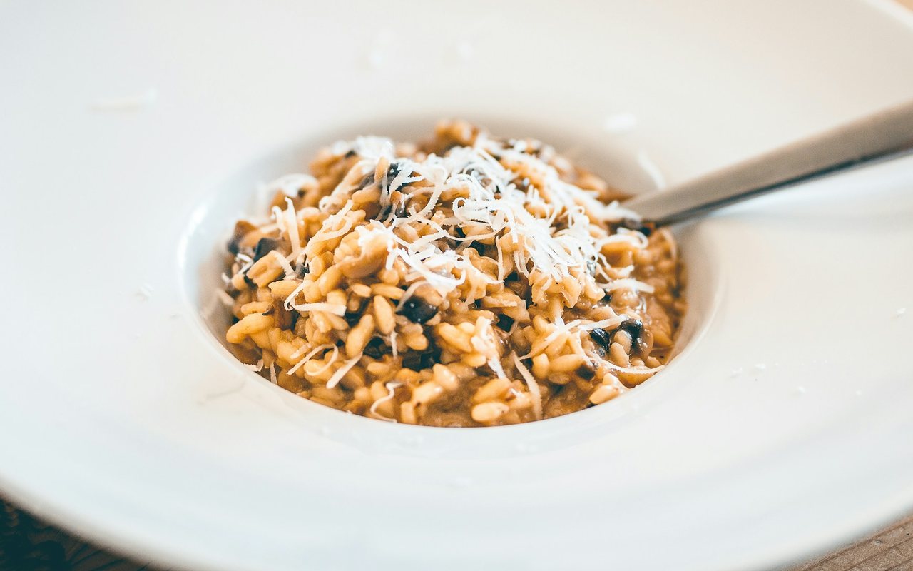 Mushroom risotto topped with grated cheese in the center of a wide white bowl.