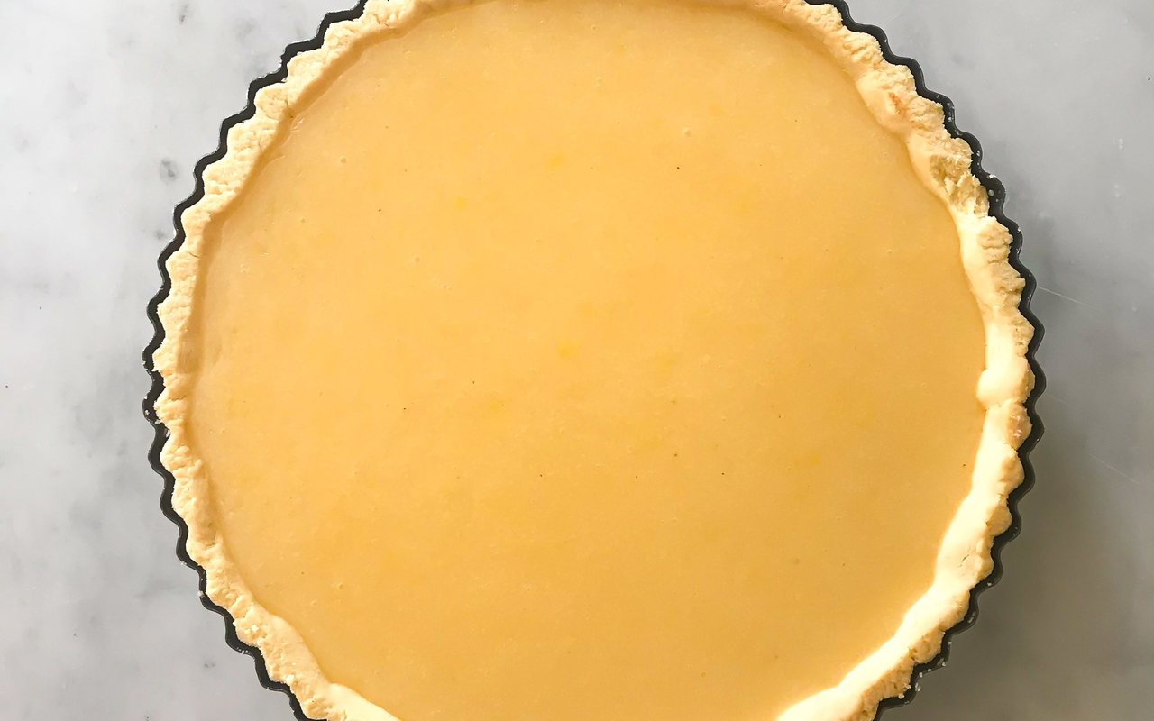 Slice of bright yellow lemon tart in a fluted pastry shell
