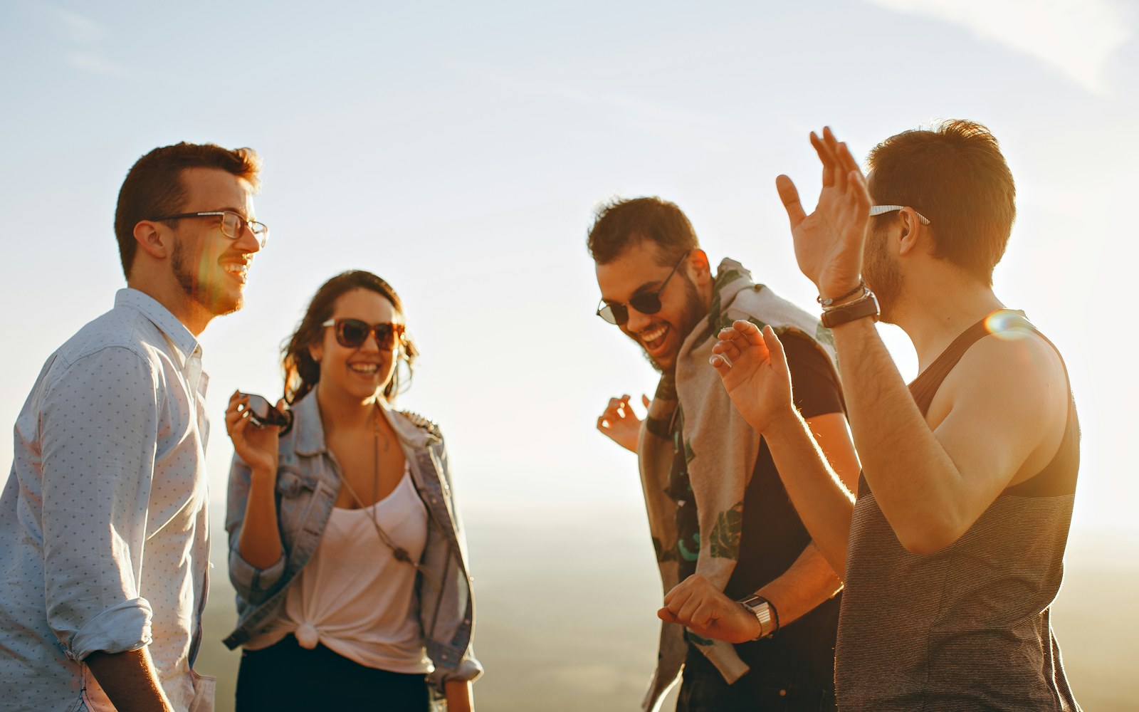 Four friends laugh together outdoors in warm sunlight