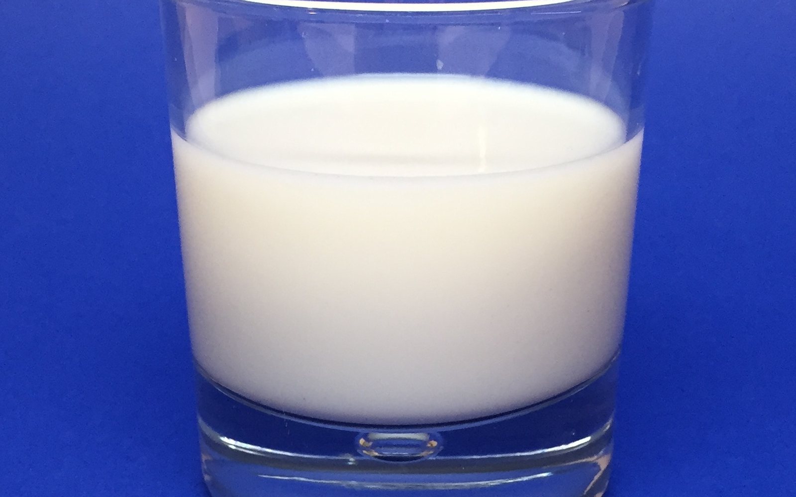 Clear glass filled with milk against a bright blue background.