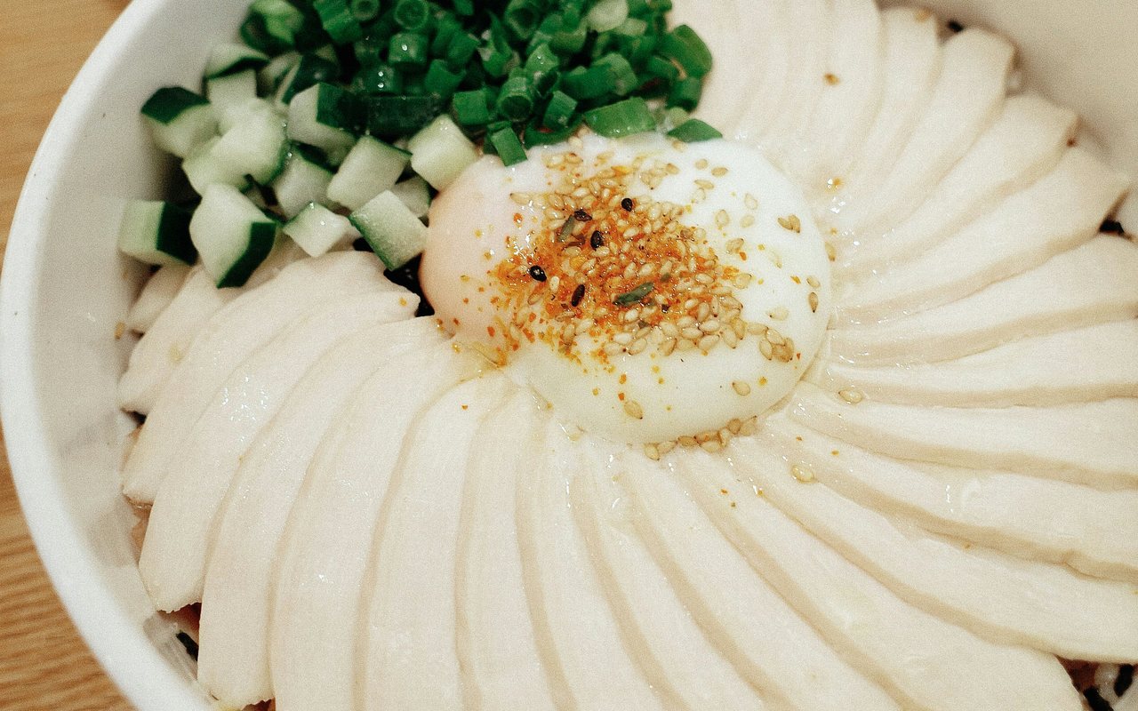 Chicken and rice bowl topped with cucumber, scallions, sesame, and a soft-cooked egg.