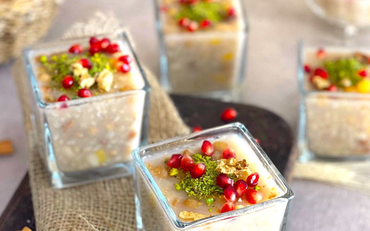 Bowls of thick aşure pudding filled with grains, beans, dried fruit, apples, and hazelnuts