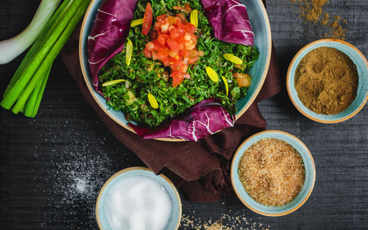 Finely chopped green herb and tomato salad arranged in a bowl with purple leaves and scallions