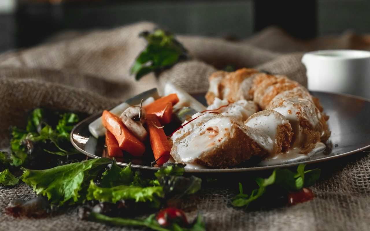Rolled chicken breast with creamy sauce, carrots, beets, and leafy vegetables.