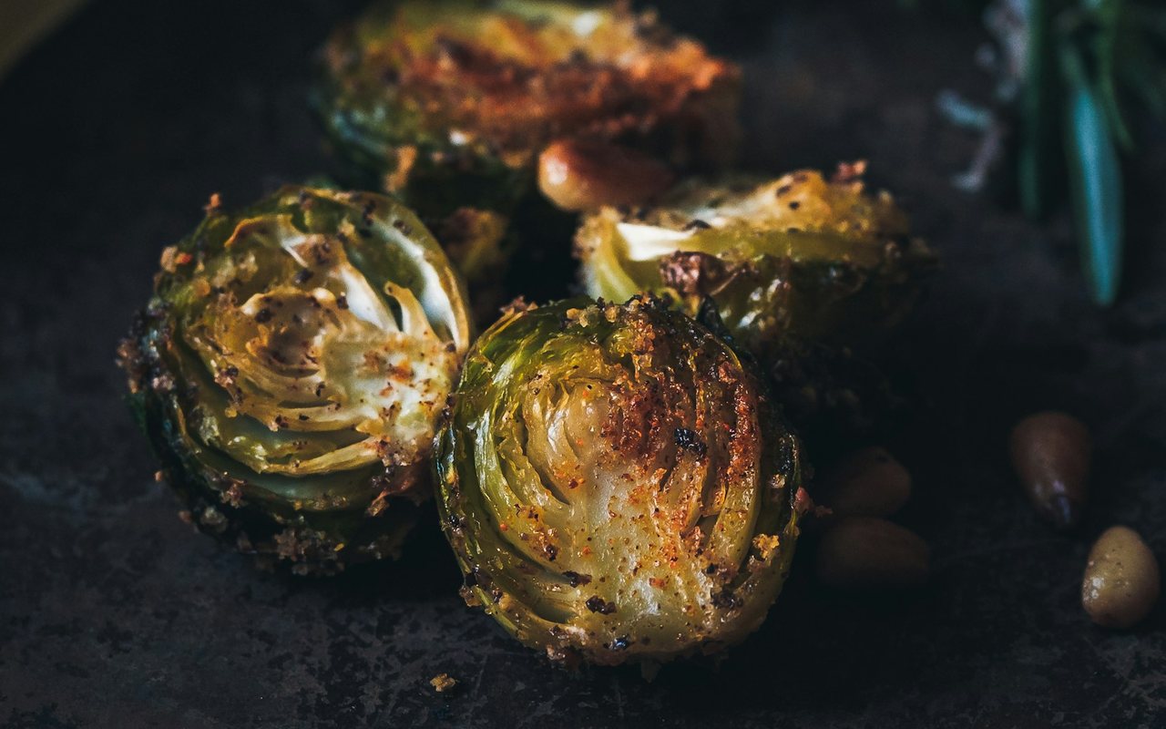 Three crispy Brussels sprout halves beside a lemon wedge and rosemary on a dark surface.